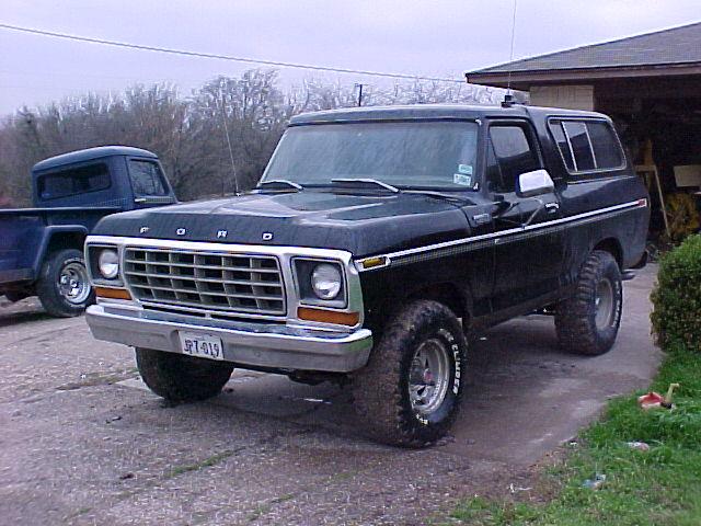 Black lifted Ford Bronco on chrome wheels parked on a driveway by a garage