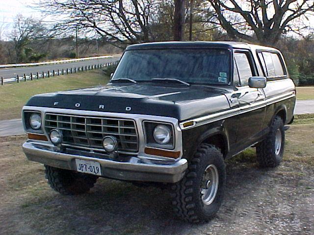 Black lifted Ford Bronco SUV with chrome grille and off-road tires, front three-quarter view, parked on grass