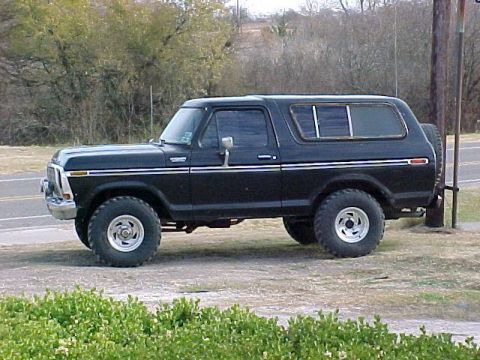1978 Ford Bronco - This black 1978 Ford Bronco is parked on a dirt area next to a road with trees in the background.