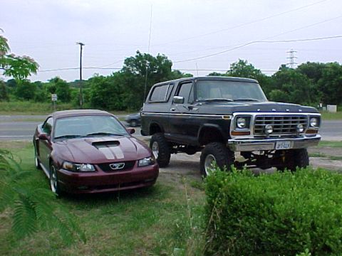 1978 Ford Bronco - A lifted black 1978 Ford Bronco is parked next to a maroon Ford Mustang on a grassy area.