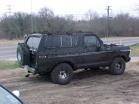 1978 Ford Bronco - A muddy 1978 Ford Bronco sits off-road, its exterior heavily coated in dirt and grime.