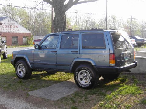 1999 Jeep Cherokee - A blue Jeep Cherokee is parked on a grassy area next to a building.