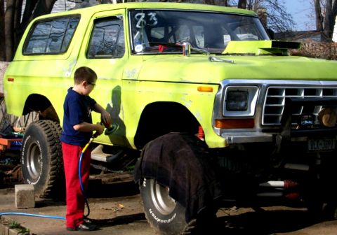 1978 Ford Bronco - A young boy polishes the side of a lifted 1978 Ford Bronco, which has a prominent hood scoop and off-road tires.