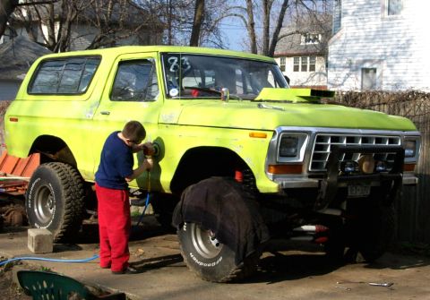 1978 Ford Bronco - A person polishes the fender of a lime green 1978 Ford Bronco with a lifted suspension and large off-road tires.