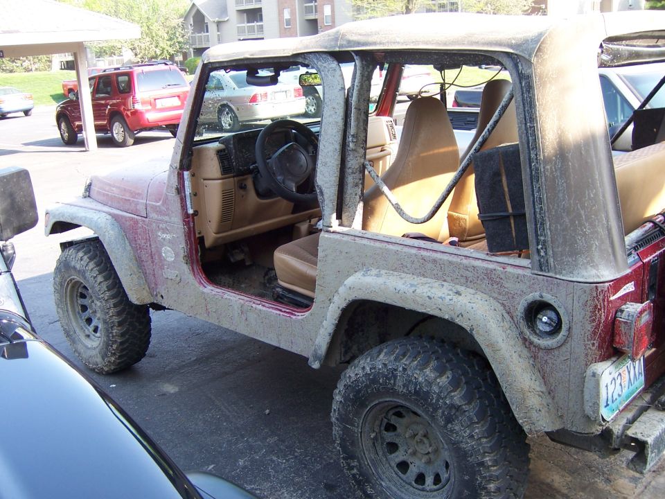 Mud-covered 1998 Jeep TJ with doors removed, parked next to another vehicle