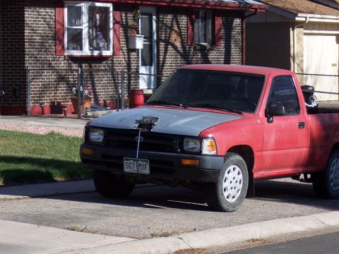 1972 Ford Ranchero - A red pickup truck with a gray hood and a camera mount is parked on a suburban street.