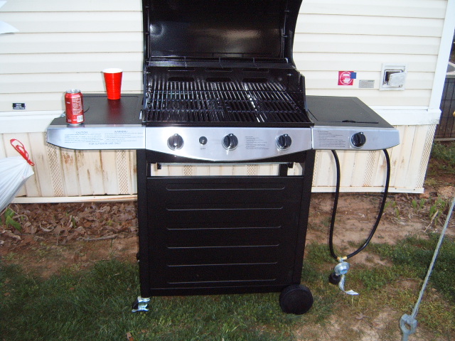 Black gas grill with red cup and can on side shelf