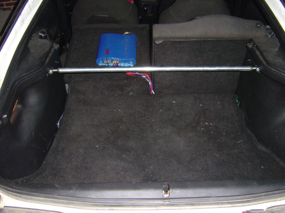 Carpeted hatchback cargo area with a chrome strut bar and blue amplifier