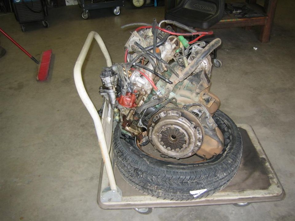 Four-cylinder engine with clutch and flywheel exposed on a shop cart