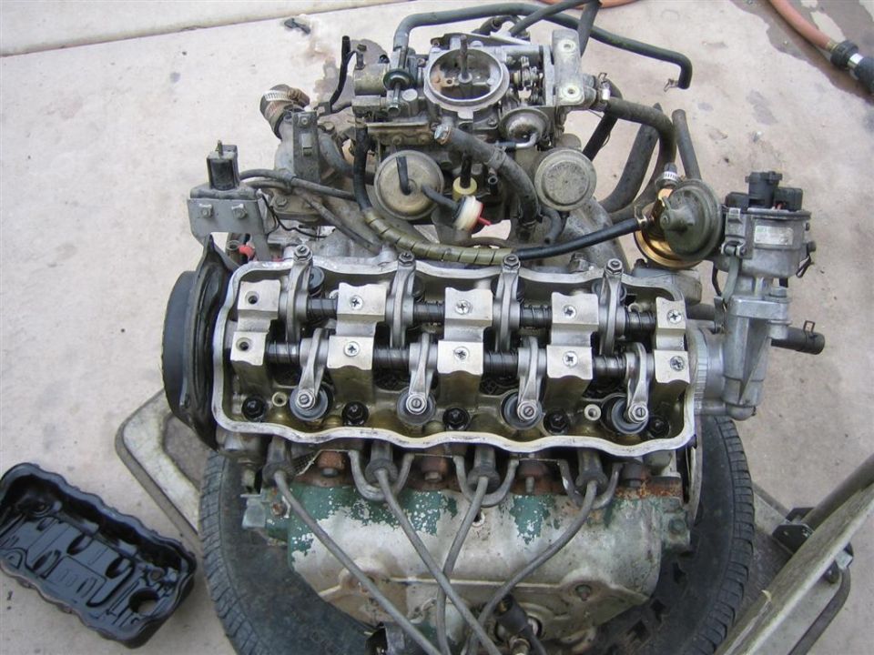 Engine with valve cover removed, showing camshaft and rockers. Carburetor and distributor are visible