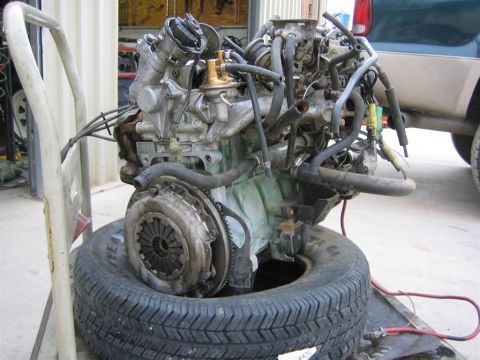 1987 Suzuki Samurai - An engine and transmission assembly is displayed on a tire, with a portion of a vehicle visible in the background.