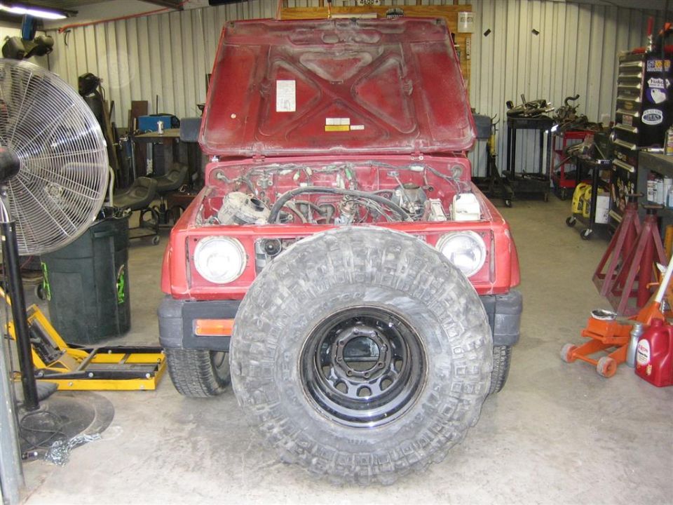 Red SUV with hood open and large tire in front