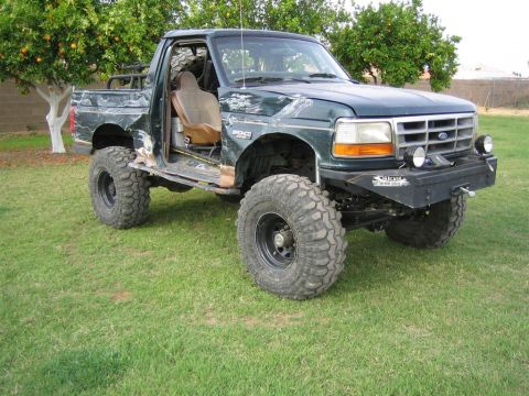 1994 Ford Bronco - This modified 1994 Ford Bronco features large off-road tires and visible body damage, suggesting it has seen extensive use.