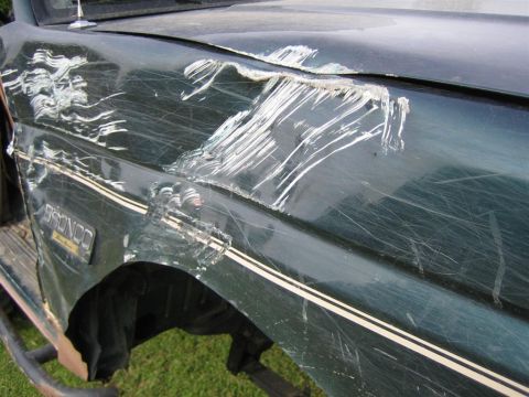 1994 Ford Bronco - The front fender and hood of a green Ford Bronco exhibit severe damage, including numerous scratches and dents.