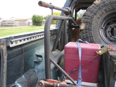 1994 Ford Bronco - The interior of a vehicle shows a roll cage, a spare tire, and a red gas can strapped down.