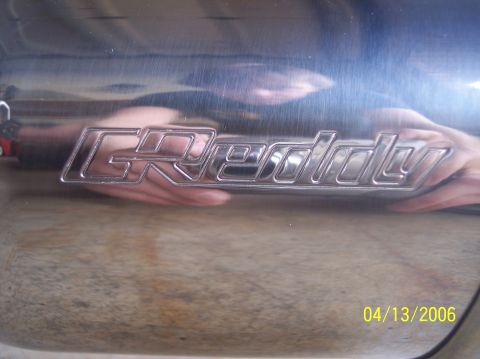 1995 Ford Probe - Close-up of a chrome GReddy exhaust tip, showing the brand name and a reflection of a hand.