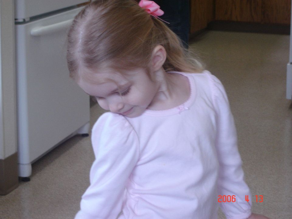 Young girl in a pink shirt looking down, with a pink bow in her hair. A white appliance is to her left