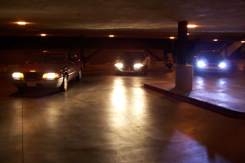 Three cars with headlights on in a dark parking garage