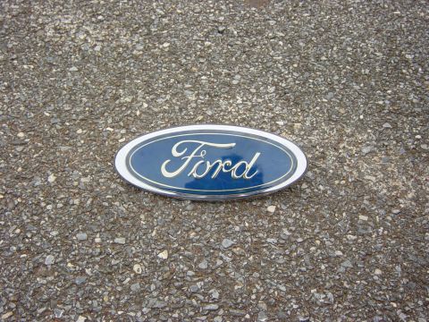 1982 Ford Crown Victoria LTD - A blue Ford oval emblem with chrome trim is shown lying on a gravelly surface.
