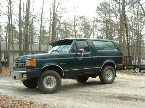 1988 Ford Bronco - Side view of a dark green Ford Bronco, model year 1987, with a trailer hitched to the rear.