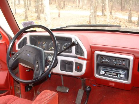 1988 Ford Bronco - The interior of a 1988 Ford Bronco shows a red dashboard, black steering wheel, and a manual transmission shifter.