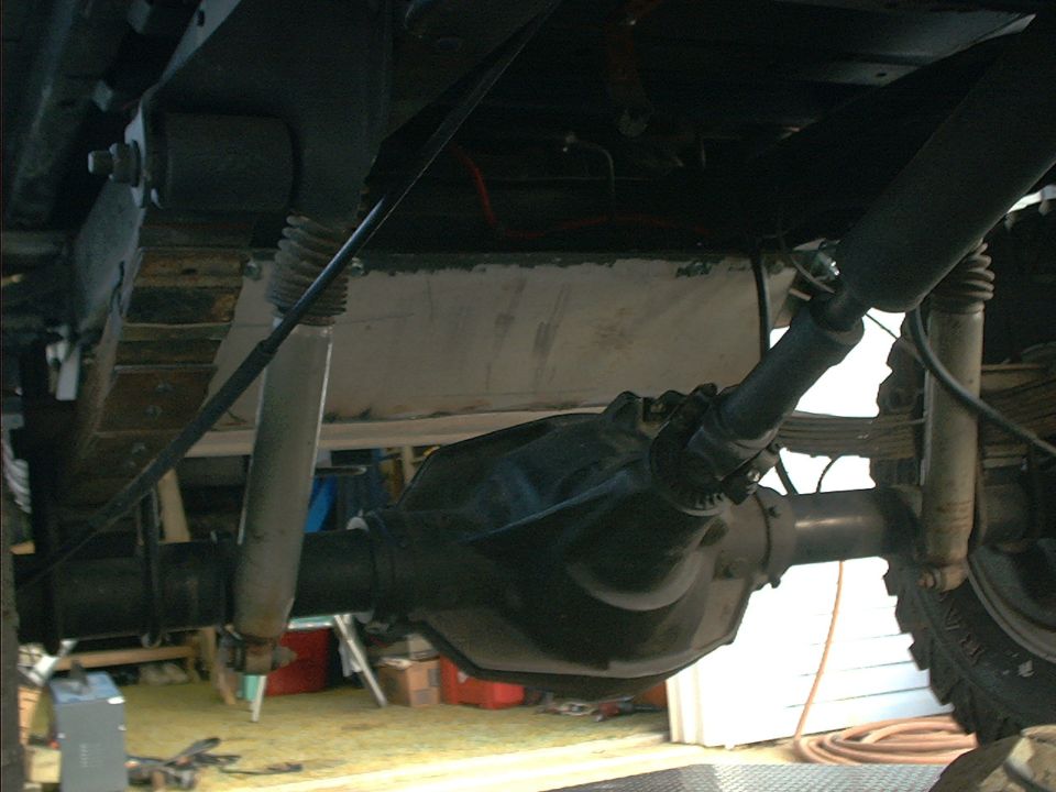 Underside view of a vehicle's rear axle, driveshaft, leaf springs, and shock absorbers