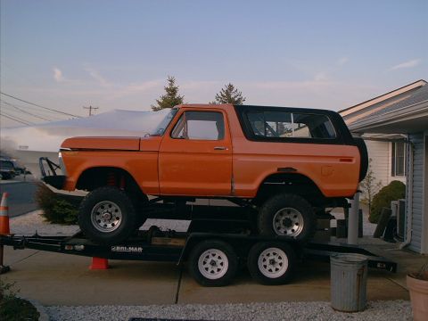 1978 Ford Bronco - An orange 1978 Ford Bronco is loaded onto a trailer in front of a residential building.