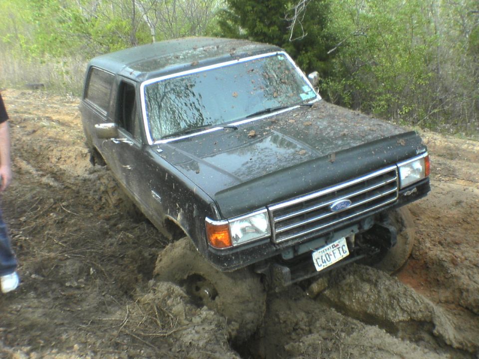 Muddy dark Ford SUV stuck in deep mud pit, front 3/4 view, Texas plate