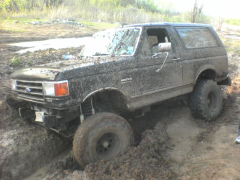 1991 Ford Bronco - A 1991 Ford Bronco is stuck in the mud, with its front-left wheel submerged.