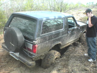 1991 Ford Bronco - A person stands by a 1991 Ford Bronco that is stuck in thick mud.
