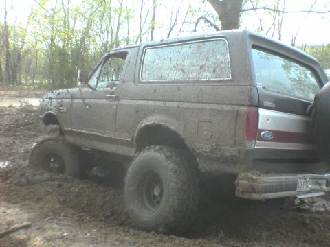 1991 Ford Bronco - This 1991 Ford Bronco is deeply stuck in thick mud, with trees and water in the background.