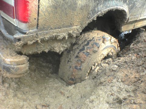 1991 Ford Bronco - This vehicle is deeply embedded in mud, with only the rear section and a tire visible.