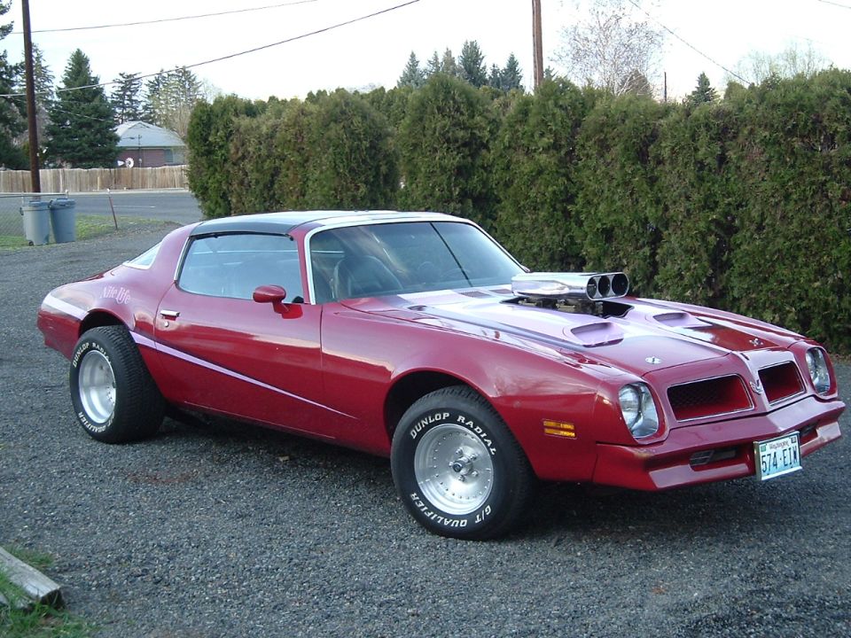 Red Pontiac Firebird coupe with hood-mounted blower scoop, front 3/4 view on gravel