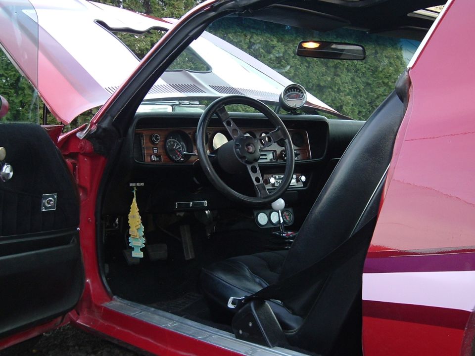 Interior of red Firebird coupe through open door with black seats and woodgrain dash