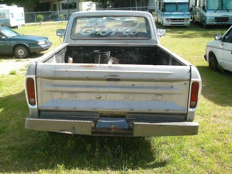 1986 Ford Bronco - Silver Ford pickup truck seen from the rear, prominent Ford lettering on the tailgate and a diamond plate bumper.