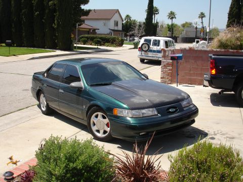 1993 Ford Taurus - A 1993 Ford Taurus is parked in a suburban driveway next to other vehicles.
