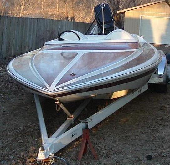 White speedboat with maroon deck striping on a trailer near a fence and shed
