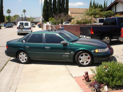 1993 Ford Taurus - A green 1993 Ford Taurus sedan is parked on a residential street next to a black pickup truck.