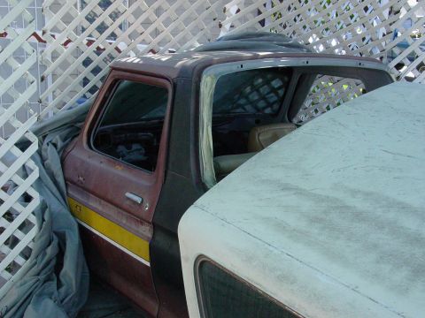 1979 Ford Bronco - Side view of a 1979 Ford Bronco cab, covered by a tarp, parked next to another vehicle.