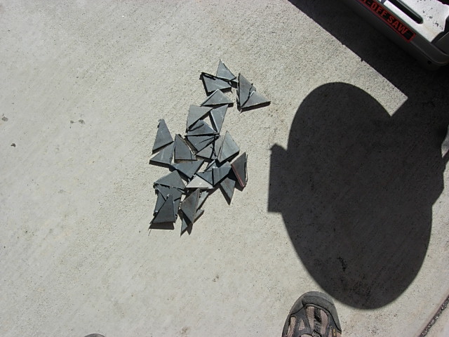 Pile of small gray triangular sheet-metal scrap pieces on concrete with photographer's shadow
