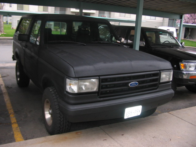 Black Ford Bronco parked under a carport, another SUV next to it