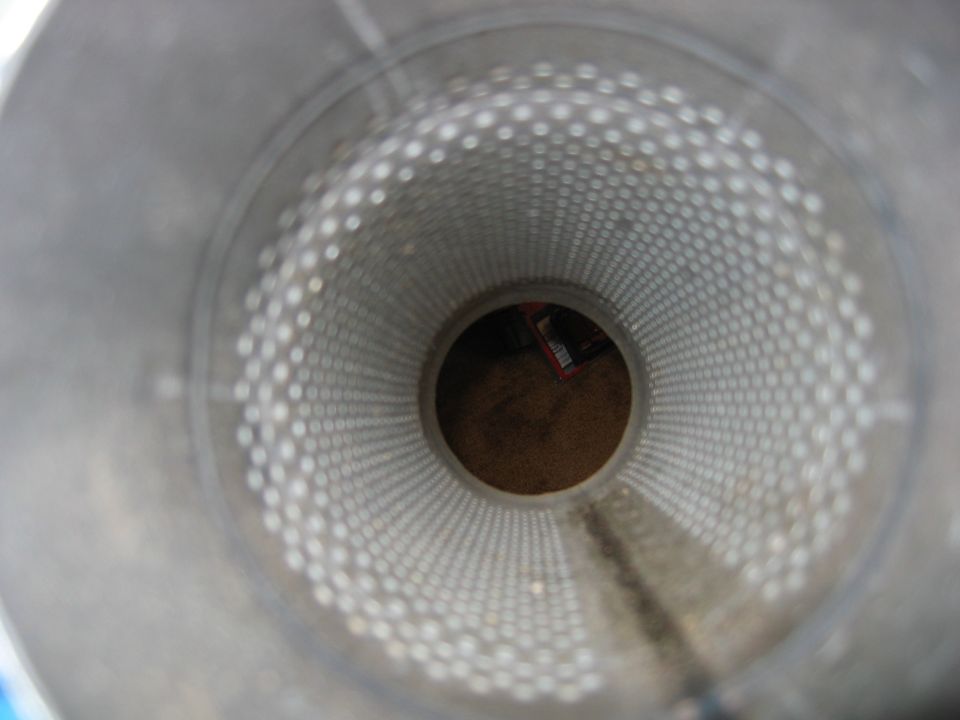 Looking down inside a cylindrical perforated metal muffler or filter housing