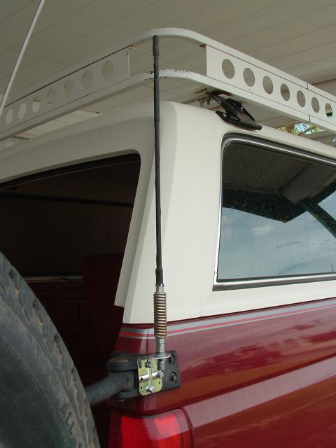1990 Ford Bronco - Rear view of a red Ford Bronco with a white camper shell and roof rack, fitted with a CB antenna.