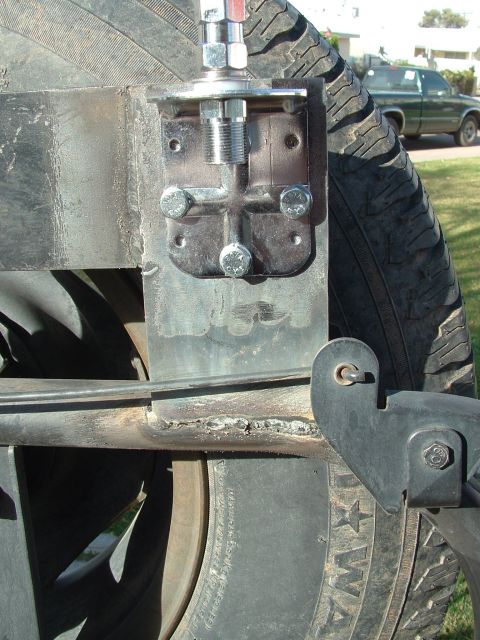 1990 Ford Bronco - Close-up of a spare tire mount and CB antenna bracket, with a green pickup truck visible in the background.