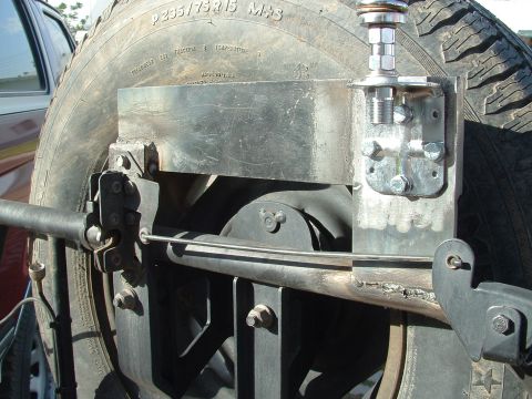 1990 Ford Bronco - Close-up of a spare tire mount and tire, with a portion of another vehicle in the background.