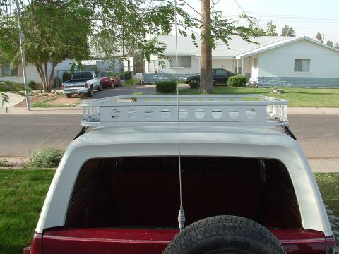 1990 Ford Bronco - Overhead-from-behind view of a white fiberglass SUV hardtop fitted with a white welded steel roof rack with punched-hole side rails, mounte…