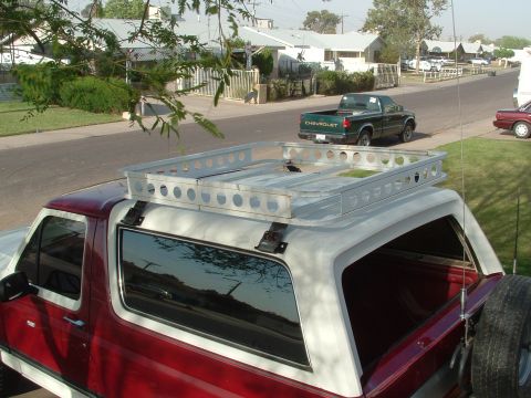 1990 Ford Bronco - Elevated rear-quarter view of a red and white Ford Bronco with a fabricated aluminum roof rack featuring rows of round lightening holes mou…