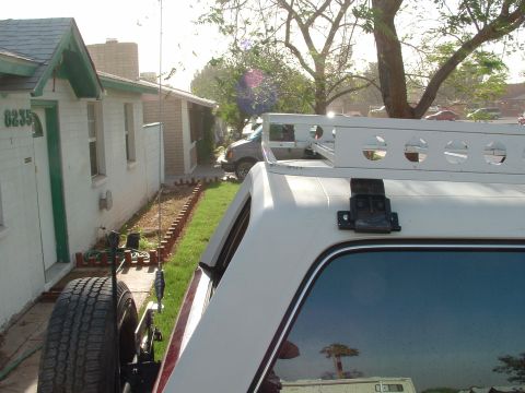 1990 Ford Bronco - Rear three-quarter close-up of a white SUV hardtop with a maroon lower body, showing a white roof rack with round lightening holes mounted…