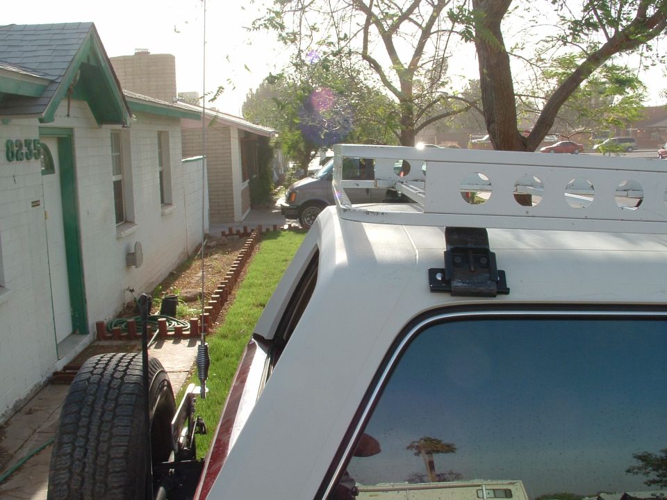 White hole-punched roof rack on black brackets above tinted rear glass of white-and-maroon SUV