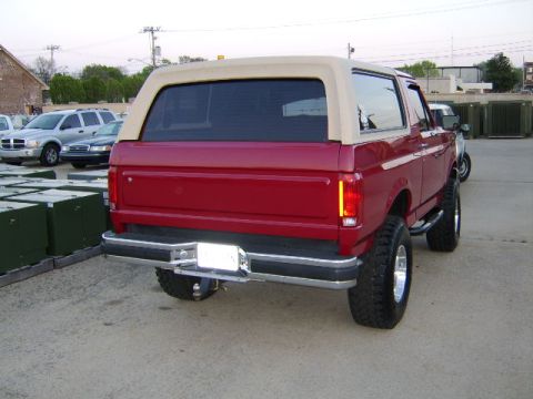 1989 Ford Bronco - Rear view of a red 1989 Ford Bronco, a tan removable top and large off-road tires.